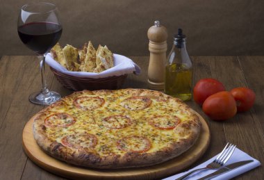 Kırmızı domates dilimli Mozzarella peynirli pizza, yanında bir bardak kırmızı şarap ve bir porsiyon crostini. Kırmızı domates, zeytinyağı ve biber öğütücü. Kompozisyonda vurgula.