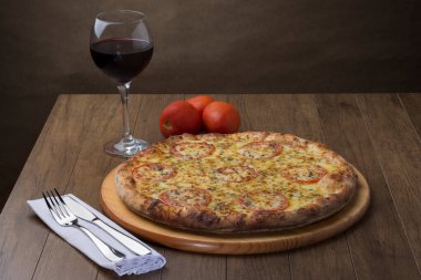 Mozzarella Peynirli Pizzanın Gastronomik fotoğrafı. Yanında da kırmızı domates dilimleri ve bir bardak kırmızı şarap. Süslemek için domates ve tatmak için çatal bıçak takımı hazır. Yatay fotoğraf.