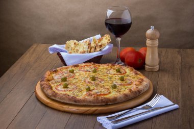 Mozzarella peynirli pizzanın kırmızı domates dilimleri ve yeşil zeytinli gurme fotoğrafı. Bir kadeh kırmızı şarap. Çatal ve bıçak tatmaya hazır..