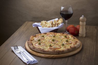 Mozzarella peynirli pizzanın kırmızı domates dilimleri ve yeşil zeytinli gurme fotoğrafı. Bir kadeh kırmızı şarap. Soldaki çatal ve bıçak tatmaya hazır..