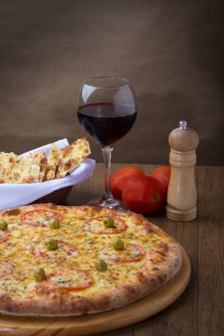 Kırmızı domates dilimleri ve yeşil zeytinli lezzetli Mozzarella peynirli pizzanın fotoğrafı. Bir kadeh kırmızı şarap. Crostini 'nin bir kısmı. Çatal ve bıçak tatmaya hazır..