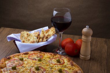 Kırmızı domates dilimleri ve yeşil zeytinli lezzetli Mozzarella peynirli pizzanın fotoğrafı. Bir kadeh kırmızı şarap. Gurme fotoğrafçılık gölgeli arkaplan.