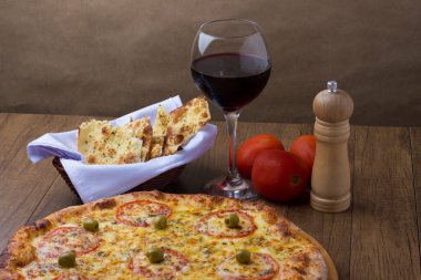 Kırmızı domates dilimleri ve yeşil zeytinli lezzetli Mozzarella peynirli pizzanın fotoğrafı. Bir kadeh kırmızı şarap. Gurme fotoğraf arkaplanı.