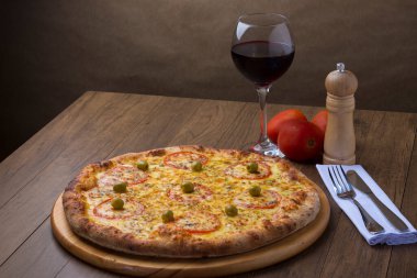 Kırmızı domates dilimleri ve yeşil zeytinli lezzetli mozarella peynirli pizzanın fotoğrafı. Bir kadeh kırmızı şarap. Süslemek için üç kırmızı domates..