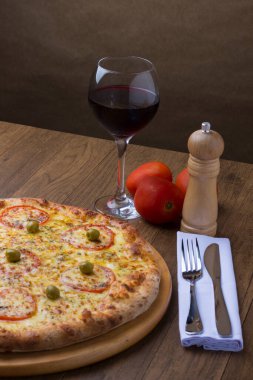 Kırmızı domates dilimleri ve yeşil zeytinli lezzetli mozarella peynirli pizzanın fotoğrafı. Bir kadeh kırmızı şarap. Süslemek için üç kırmızı domates. Dikey fotoğraf.