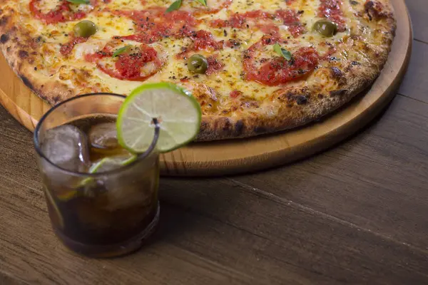 Pizza Marguerita made with tasty pizza dough, Mozzarella, tomatoes, marjoram and green olives. On the wooden board. Napolitan Pizza. cup with cola and ice soda. Made by the best pizzerias in the world