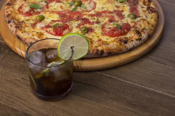 Pizza Marguerita made with tasty pizza dough, Mozzarella, tomatoes, marjoram and green olives. On the wooden board. Napolitan Pizza. Glass with cola and ice soda. Open horizontal photo.