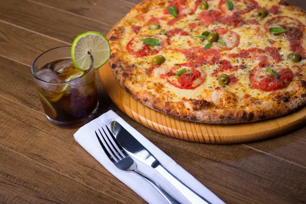 Close-up view of Pizza Marguerita made with, Mozzarella, cheeses, tomatoes, macaroni and green olives. Traditional Neapolitan Pizza. Glass with cola soft drink, Italian cuisine.