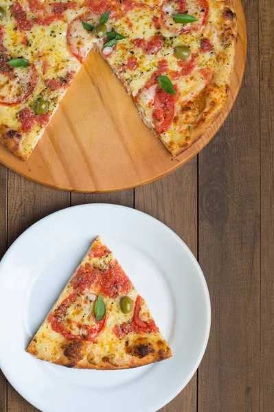 Mozzarella peyniri, domates, fesleğen yaprağı ve yeşil zeytinlerle yapılmış pizza Marguerita 'nın fotoğrafı ahşap bir tahtada servis ediliyor. Tabakta servis edilen pizza dilimi. Üst Makro Fotoğrafçılık.