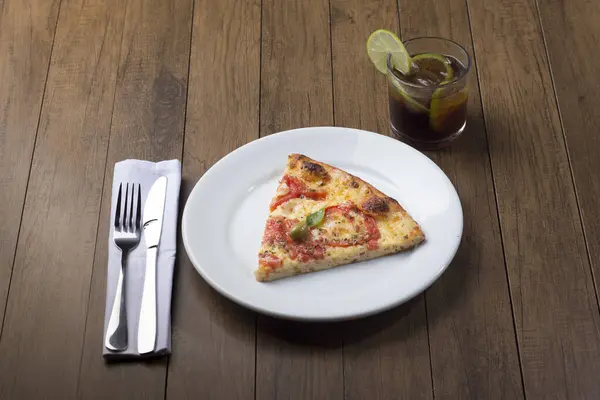 Photograph of a tasty Pizza Marguerita made with Mozzarella Cheese, tomatoes, basil leaves and green olives. Pizza slice served on white plate. Cola and lemon soda.