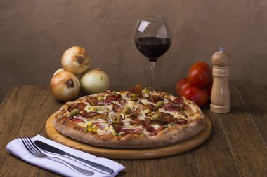 Jambon, bezelye yumurtası, palmiye, pepperoni, soğan, mozzarella ve pastırmadan yapılmış Portekiz pizzası. Yemeklere eşlik etmesi için tahta bir tahtada kırmızı şarapla servis edilmiş. Çatal ve bıçak..