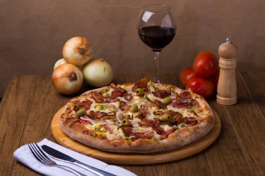 Jambon, bezelye yumurtası, palmiye, pepperoni, soğan, mozzarella ve pastırmadan yapılmış Portekiz pizzası. Yemeklere eşlik etmesi için tahta bir tahtada kırmızı şarapla servis edilmiş. Yakın plan fotoğraf..