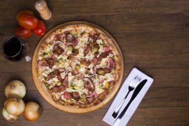 Lezzetli Portekiz pizzası jambon, bezelye yumurtası, palmiye, pepperoni, soğan, mozzarella ve pastırmadan yapılmış. Tahta tahtada servis edilmiş. Üst yakın plan fotoğraf. Bir kadeh kırmızı şarap. Metin için boşluk.