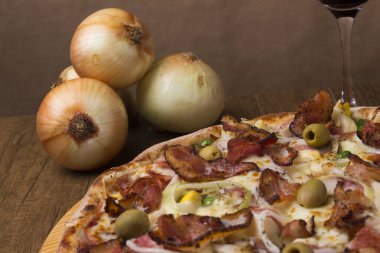 Jambon, bezelye yumurtası, palmiye, pepperoni, soğan, mozzarella ve pastırmadan yapılmış Portekiz pizzası. Sahneyi oluşturmak için taşralı soğanlar. Gastronominin yakın plan fotoğrafı.