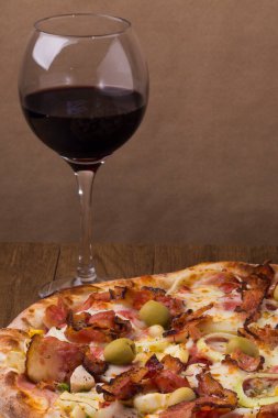 Jambon, bezelye yumurtası, palmiye, pepperoni, soğan, mozzarella ve pastırmadan yapılmış Portekiz pizzası. Bir kadeh kırmızı şarap. Dikey gastronomik fotoğrafçılık.