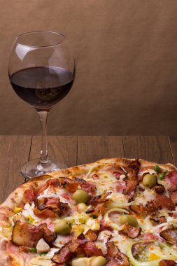 Lezzetli Portekiz pizzası jambon, bezelye yumurtası, palmiye, pepperoni, soğan, mozzarella ve pastırmadan yapılmış. Bir kadeh kırmızı şarap. Metin için sağ üst boşluğu olan dikey gastronomik fotoğraf.