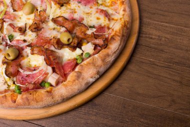 Jambon, bezelye yumurtası, palmiye, pepperoni, soğan, mozzarella ve pastırmadan yapılmış Portekiz pizzası. Tahta bir tahtanın üzerinde servis edilmiş. Sağ taraftaki metin için yeri olan yakın plan fotoğraf.