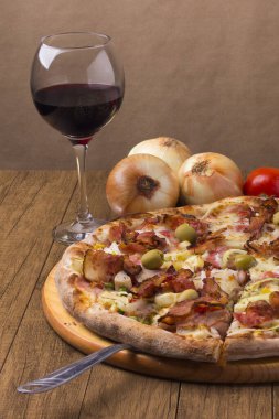 Jambon, bezelye yumurtası, palmiye, pepperoni, soğan, mozzarella ve pastırmadan yapılmış Portekiz pizzası. Bir kadeh kırmızı şarap. Pizza dilimi servis etmek için kesilmiş. Pizzacıların gurme fotoğrafı.