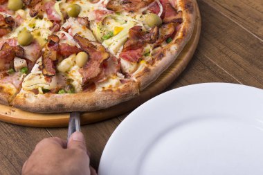 Jambon, bezelye yumurtası, palmiye, pepperoni, soğan, mozzarella ve pastırmadan yapılmış Portekiz pizzası. Spatulalı pizza servisi. Restoranların ve pizzacıların gastronomik fotoğrafları.