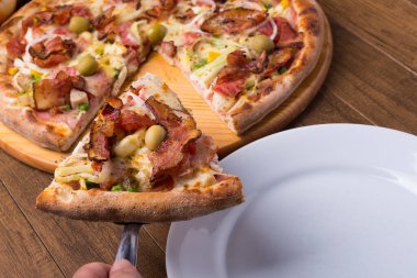 Jambon, bezelye yumurtası, palmiye, pepperoni, soğan, mozzarella ve pastırmadan yapılmış Portekiz pizzası. Tabakta servis edilen bir dilim pizza. Restoranların ve pizzacıların fotoğrafı.