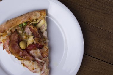 Tabakta servis edilen pizza dilimi. Jambon, bezelye yumurtası, palmiye, pepperoni, soğan, mozzarella ve pastırmadan yapılmış Portekiz pizzası. Üst yakın plan fotoğraf. Sağdaki metinler için boşluk.