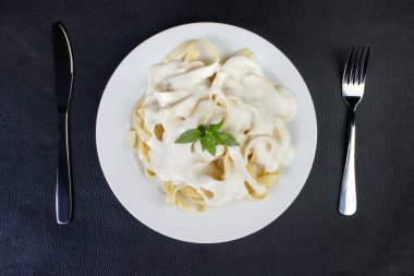 Beşamel soslu ve fesleğen yapraklı Tagliatelle makarnası. Beyaz soslu makarna. Üst görüntü fotoğrafı. Mesaj için yer var. Siyah arkaplan