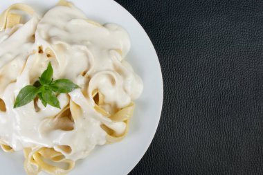 Beşamel soslu ve fesleğen yapraklı Tagliatelle makarnası. Beyaz soslu makarna. Beyaz tabakta servis edilmiş. Sağ taraftaki metinler için boş alanı olan yakın plan fotoğraf.