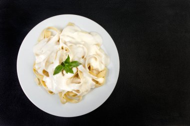 Beşamel soslu ve fesleğen yapraklı Tagliatelle makarnası. Beyaz soslu makarna. Üst görüntü fotoğrafı. Mesaj için yer var. Siyah arkaplan