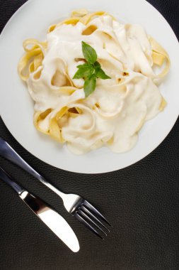 Bechamel Sauce ve Basil Leaves ile servis edilen Lezzetli Tagliatelle Pasta. Beyaz soslu makarna. Siyah desenli arkaplanı olan üst fotoğraf tomografisi.