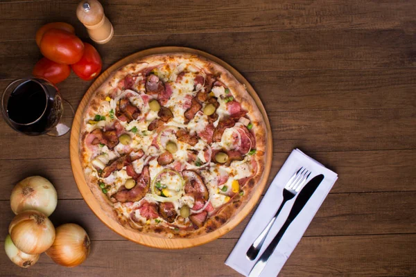 Lezzetli Portekiz pizzası jambon, bezelye yumurtası, palmiye, pepperoni, soğan, mozzarella ve pastırmadan yapılmış. Tahta tahtada servis edilmiş. Üst yakın plan fotoğraf. Bir kadeh kırmızı şarap. Metin için boşluk.