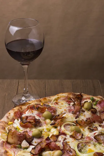 Lezzetli Portekiz pizzası jambon, bezelye yumurtası, palmiye, pepperoni, soğan, mozzarella ve pastırmadan yapılmış. Bir kadeh kırmızı şarap. Metin için sağ üst boşluğu olan dikey gastronomik fotoğraf.