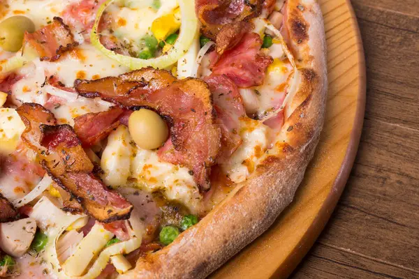Jambon, bezelye yumurtası, palmiye, pepperoni, soğan, mozzarella ve pastırmadan yapılmış Portekiz pizzası. Tahta bir tahtanın üzerinde servis edilmiş. Gurme yakın çekim fotoğrafçılık.