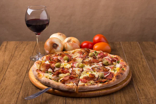 Lezzetli Portekiz pizzası jambon, bezelye yumurtası, palmiye, pepperoni, soğan, mozzarella ve pastırmadan yapılmış. Bir kadeh kırmızı şarap. Bir dilim pizza servis etmeye hazır. Pizzaların gastronomi fotoğrafı.