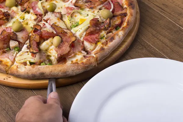 Jambon, bezelye yumurtası, palmiye, pepperoni, soğan, mozzarella ve pastırmadan yapılmış Portekiz pizzası. Spatulalı pizza servisi. Restoranların ve pizzacıların gastronomik fotoğrafları.