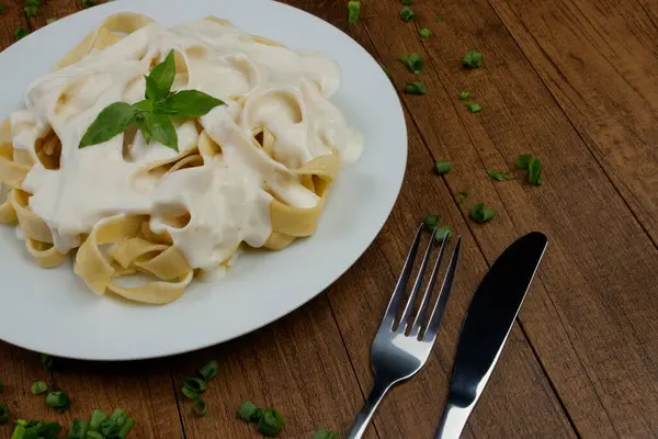 Beşamel soslu ve fesleğen yapraklı Tagliatelle makarnası. Beyaz soslu makarna. Beyaz bir tabakta servis edildi..