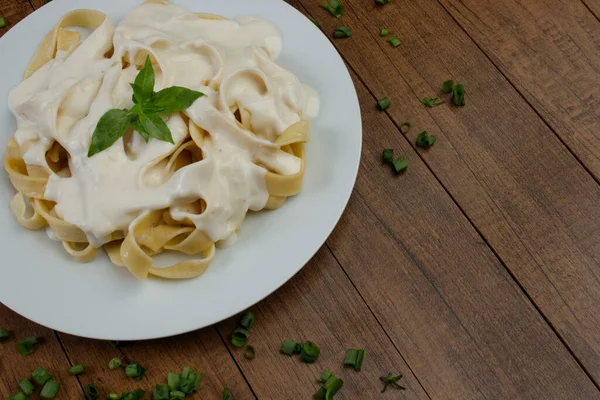 Tagliatelle pasta served with bechamel sauce and basil leaves. Pasta with white sauce. Photo gastronomy of pasta. Photo with free space for text.