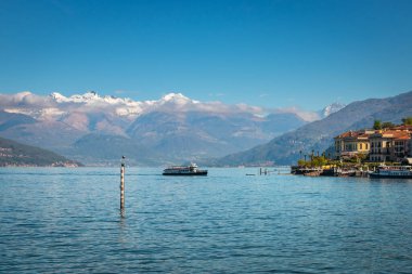 İtalya, Como Gölü manzaralı Bellagio 'ya giden feribot ve mavi gökyüzüne bakan karlı dağlar.