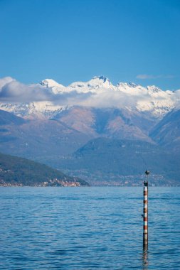İtalya 'nın Como Gölü manzaralı kırmızı-beyaz direkli ve kar kaplı dağları mavi gökyüzüne karşı