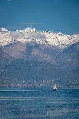 Como Gölü 'nün manzarası, İtalya ve kuzey kolu bir yelkenli teknesi ve arka planda mavi gökyüzüne karşı karla kaplı dağlarla kuzeye bakıyor.