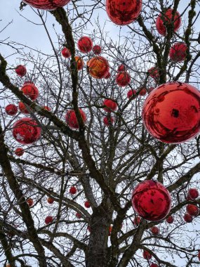 Büyük kırmızı toplar, karla kaplı Noel süslemesi gibi, açık havada bulutlu gökyüzüne karşı.