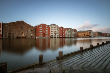 Norveç 'in Trondheim bölgesindeki Brygge bölgesinde Nidelva Nehri ile birlikte mavi gökyüzüne karşı renkli tarihi kereste depolarının uzun süre korunması