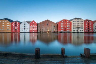 Norveç 'in Trondheim bölgesindeki Brygge bölgesinde Nidelva Nehri ile birlikte mavi gökyüzüne karşı renkli tarihi kereste depolarının uzun süre korunması