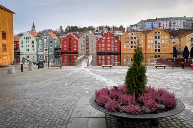 Colorful historic timber storehouses with Nidelva River in the Brygge district of Trondheim, Norway in winter against cloudy sky clipart