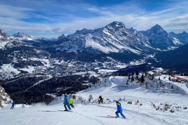 Kışın mavi gökyüzüne karşı Ampezzo Vadisi ve Monte Sorapiss Dağı ve Antelao 'nun panoramik manzarasıyla kayak yapan insanlar