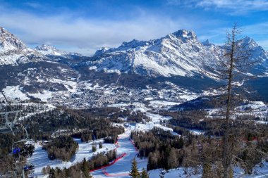 Scenic view of Tofana ski racing slope in Cortina d'Ampezzo in Italy against snow covered Punta Sorapiss Mountain and blue sky clipart