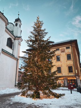 Cortina d 'Ampezzo, İtalya - 26 Ocak 2023: Mavi gökyüzüne karşı Katolik Kilisesi Santi Filippo ve Giacomo Apostoli ile aydınlatılmış Noel ağacı