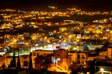 Ürdün 'ün karanlık gökyüzüne karşı aydınlanmış Wadi Musa kentinin panoramik manzarası