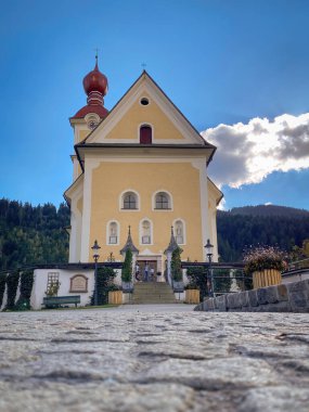 Gidiyor, Avusturya - 10 Ekim 2021: Go am Wilden Kaiser 'daki küçük kilisenin alçak açılı görüntüsü bulutlu mavi gökyüzüne karşı