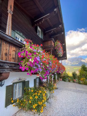 Wilder Kaiser dağlarının manzarasında eski bir çiftlik evinin balkonunda çiçeklerin açtığı, Avusturya 'nın mavi gökyüzüne karşı bulutlar.