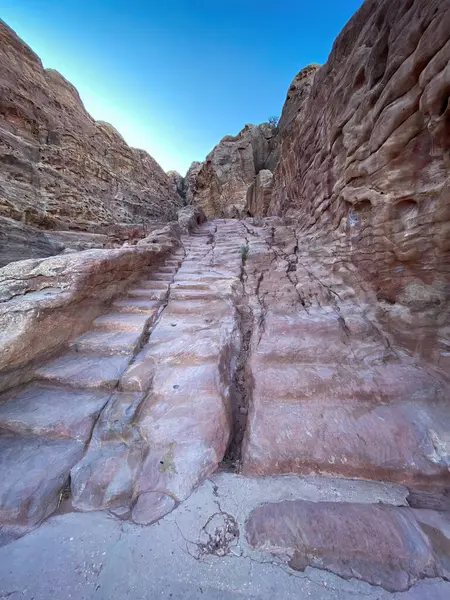 Stairs in the rock along Al-Kubtha Trail (Indiana Jones Trail) leading to Al-Khazneh Treasury in the historic and archaeological city of Petra, Jordan against blue sky